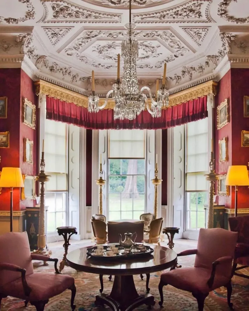 Grand formal sitting room in a British country house with red walls, an ornate ceiling, and a large chandelier.