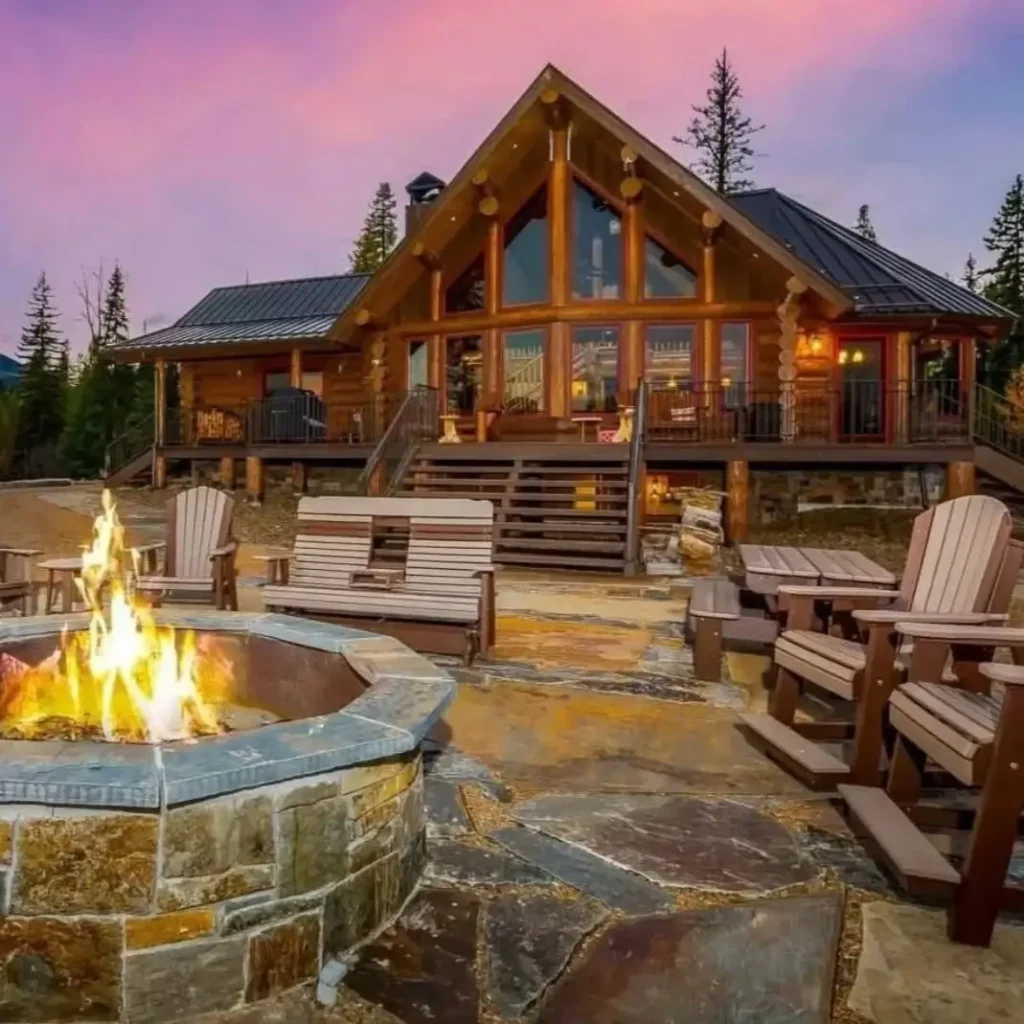 Embracing Grandeur: 25 Inspiring Ideas for Large Log Cabin Homes 14 A large log cabin home with a stone fire pit on a flagstone patio, surrounded by chairs at sunset.