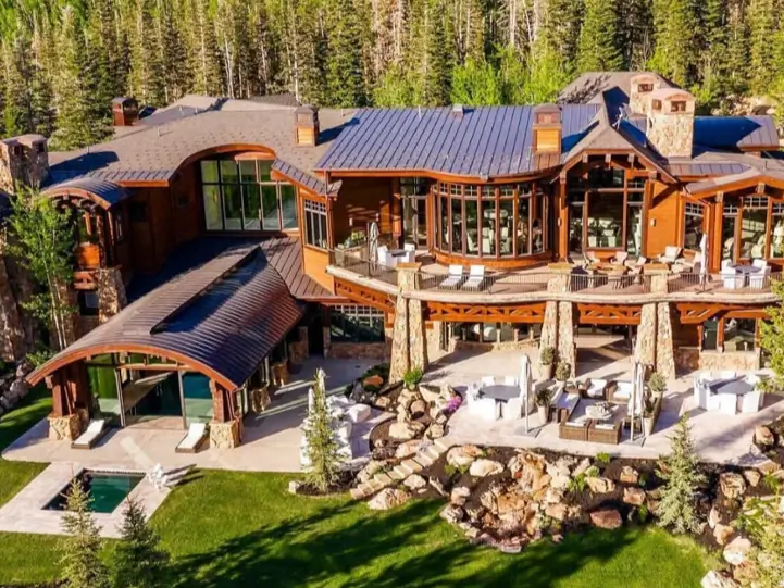 16 Mountain Mansions That Define Luxury Alpine Living 15 An aerial view of a sprawling mountain mansion designed to complement nature, with curved rooflines that echo the surrounding forested hills.