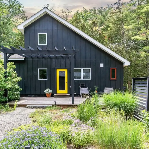 A sophisticated black house design featuring a bright yellow front door as a playful, colorful accent.