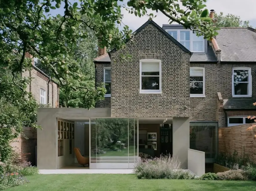 A modern concrete extension with floor-to-ceiling glass doors on the back of a traditional brick house.