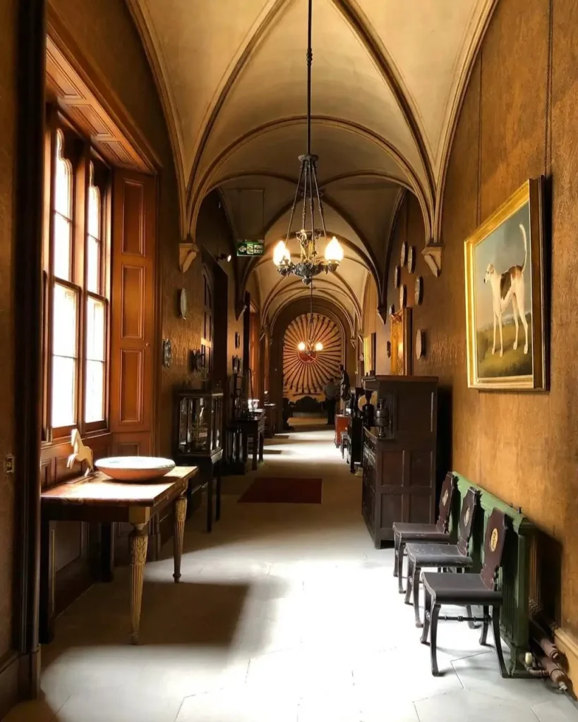 A long, vaulted hallway in a historic British country house, lined with antique furniture and artwork.