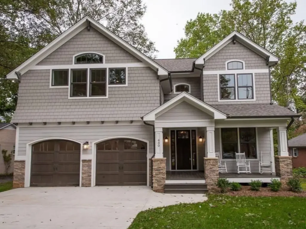 A modern craftsman house exterior with gray siding, stone accents, and wood-look garage doors.
