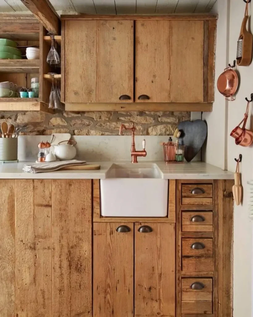 A simple rustic kitchen design featuring unfinished wood cabinets, a rough stone backsplash, and warm copper hardware.