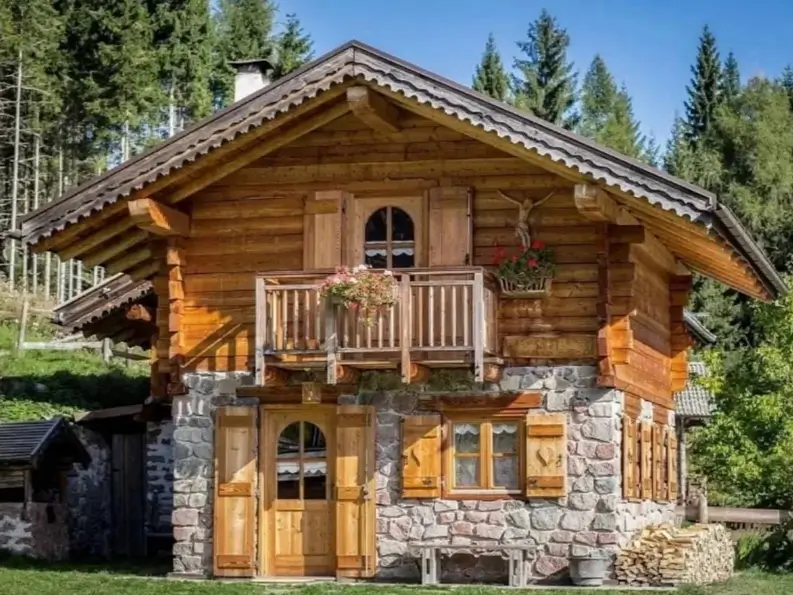 60 Charming Small Log Cabin Ideas to Inspire Your Rustic Retreat 14 A two-story small log cabin with a stone first floor and a wooden second floor with a balcony and shutters.