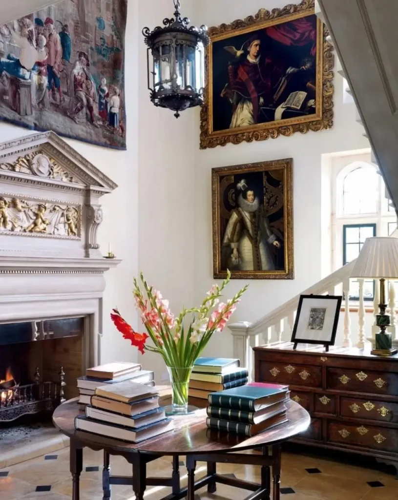 An elegant entryway in an English country home with a grand fireplace, large portraits, and a table of books.