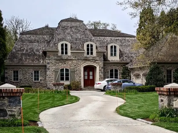 20 Stone Mansion Ideas for Classic & Modern Designs 15 A French country-style stone mansion with a wood shingle roof, arched dormer windows, and a winding driveway.