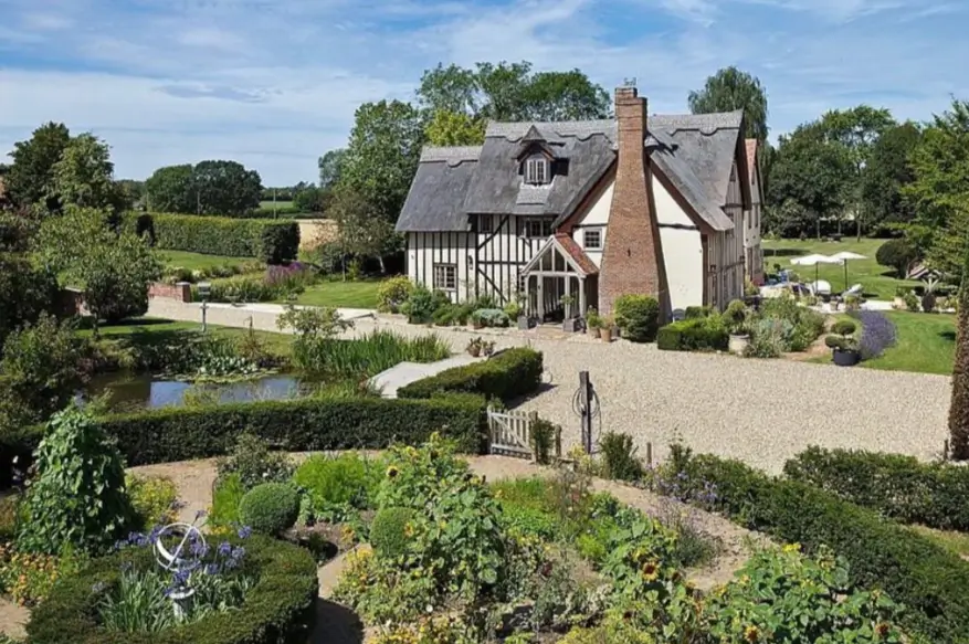 A grand country house design featuring a thatched roof, formal gardens, and a private pond on a large estate.