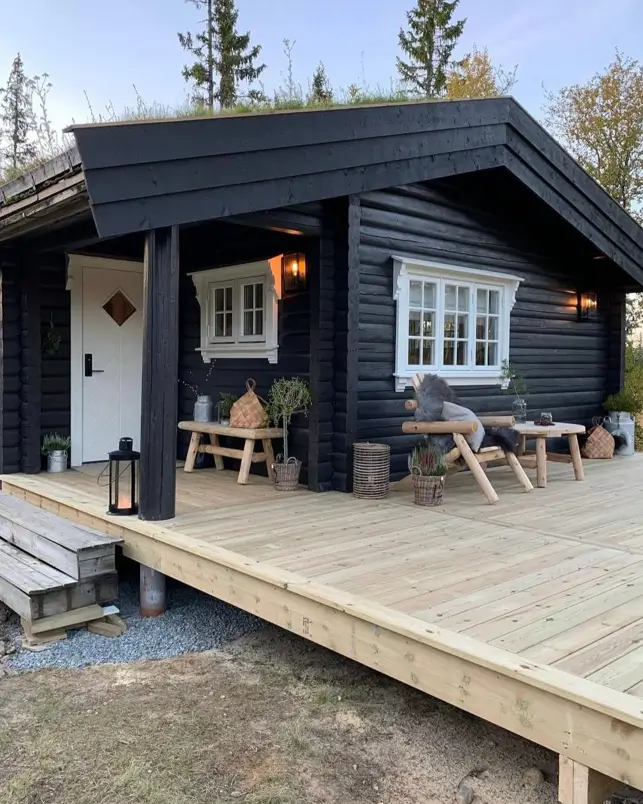 Small Log Cabins: 36 Ideas for Cozy Living & Enduring Charm 16 A modern small log cabin painted black with a spacious wooden deck and a green sod roof.
