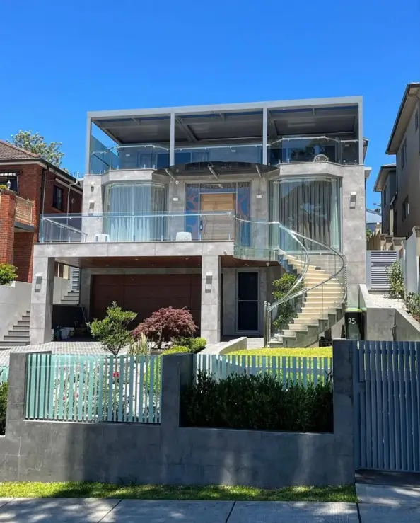 A contemporary brutalist house with a concrete facade, elegantly refined with curved glass balconies and a delicate external glass spiral staircase.