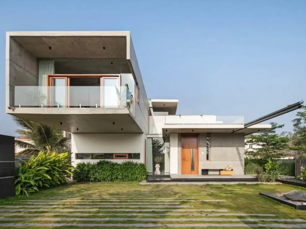 A modern concrete house featuring a dramatic cantilevered second floor with a glass balcony over a manicured lawn.