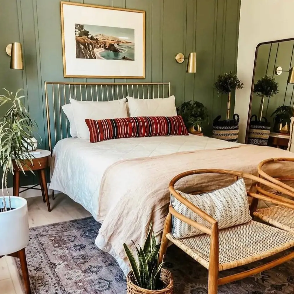A modern boho bedroom with an olive green, vertically paneled accent wall, a brass bed frame, and a large framed coastal photograph.