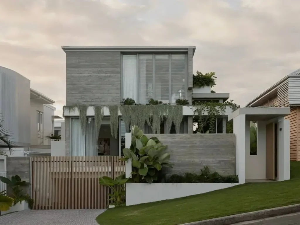 The facade of a modern brutalist house, showing a contrast between textured board-formed concrete and the warm, natural lines of a vertical wood slat gate.