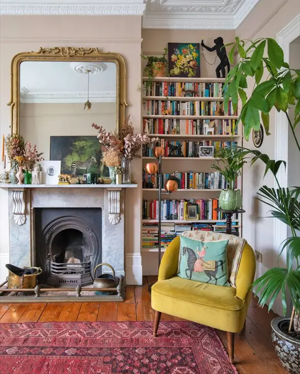 Cozy living room in an English country home featuring a marble fireplace, a yellow armchair, and shelves filled with books.