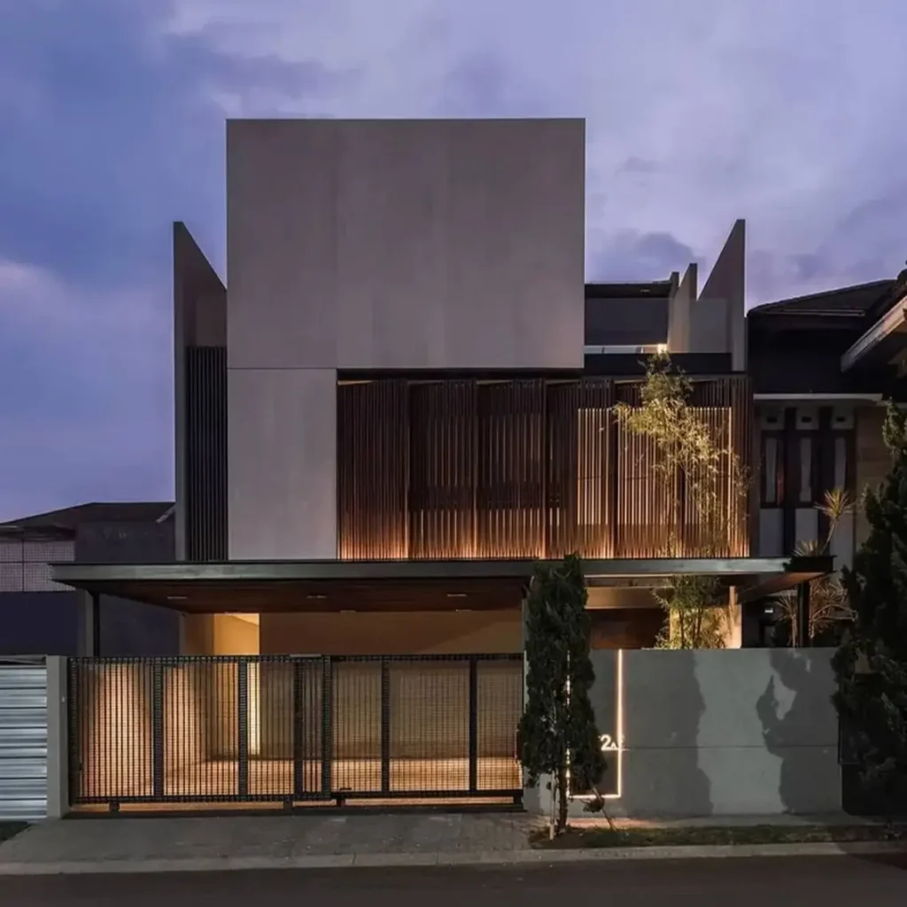 A modern concrete home at dusk, with warm light illuminating a dark slatted screen on its facade.
