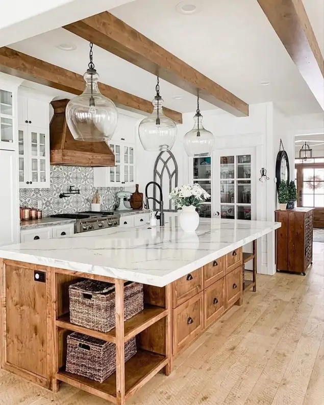 A modern rustic farmhouse kitchen with a large natural wood island, white cabinets, and oversized glass pendant lights.