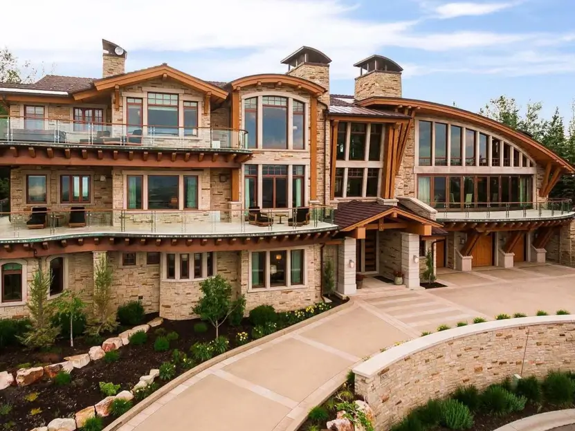 16 Mountain Mansions That Define Luxury Alpine Living 18 A sophisticated mountain mansion blending rustic light-toned stonework with the sleek, modern look of glass balcony railings.