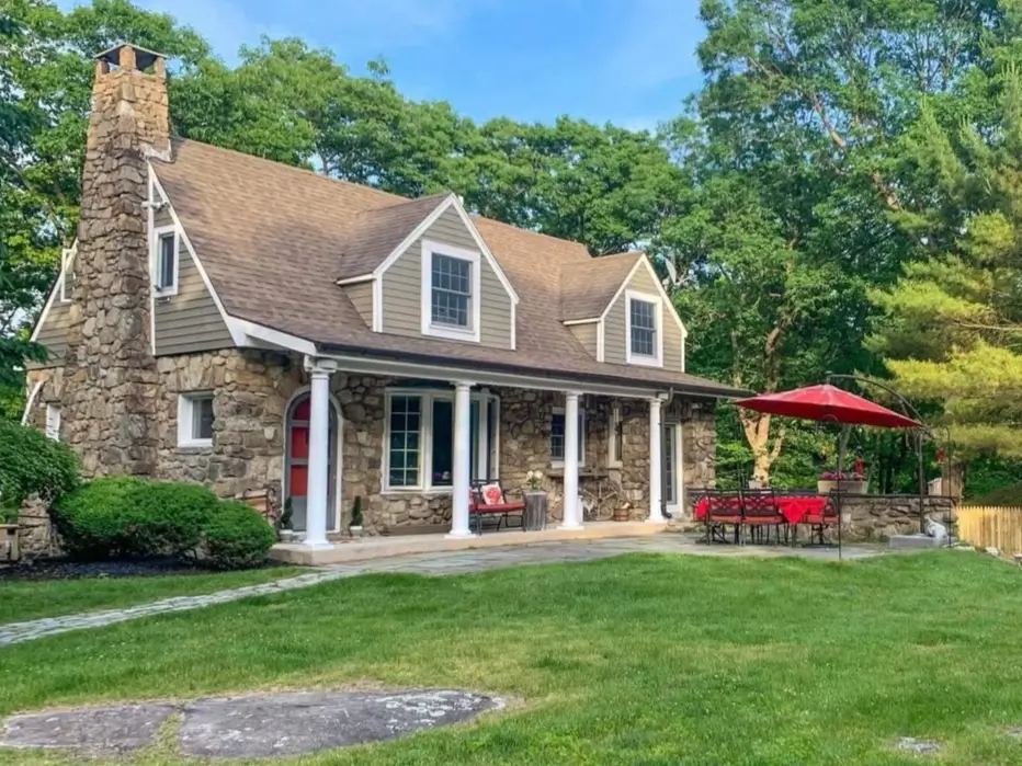 A stone cottage house with a large covered front porch, stone patio, and green siding.