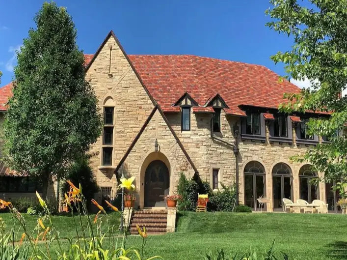 20 Stone Mansion Ideas for Classic & Modern Designs 16 A beautiful stone mansion featuring a steep, red terracotta tile roof and arched windows, set on a lush green lawn.