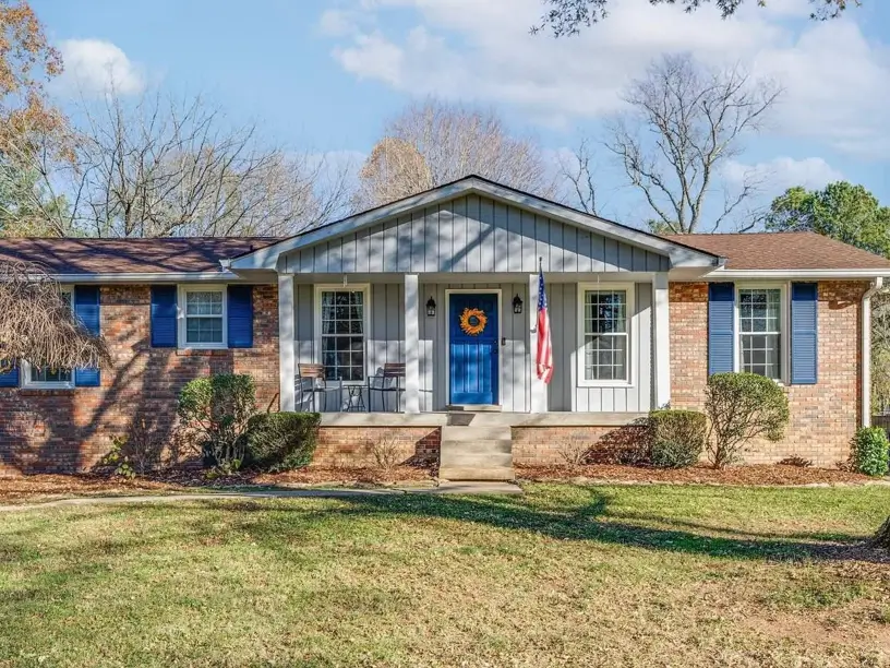 A brick ranch house with a gray gabled portico and a bright blue front door and shutters.