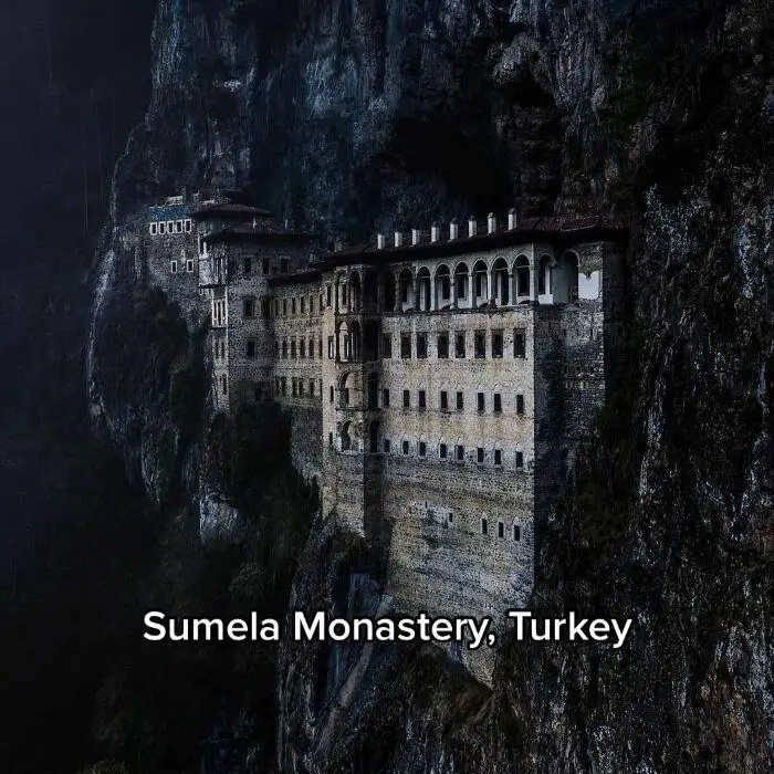An ancient stone building integrated directly into a sheer rock cliff face, a dramatic architectural concept.