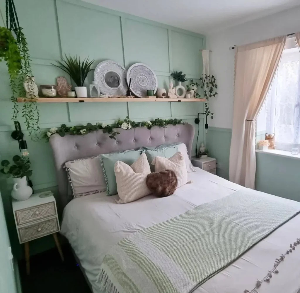 A cozy bedroom featuring a sage green paneled accent wall behind a gray tufted bed with decorative pillows.