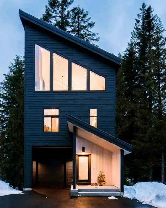 A modern black house featuring a dynamic, asymmetrical roofline and large angular windows.