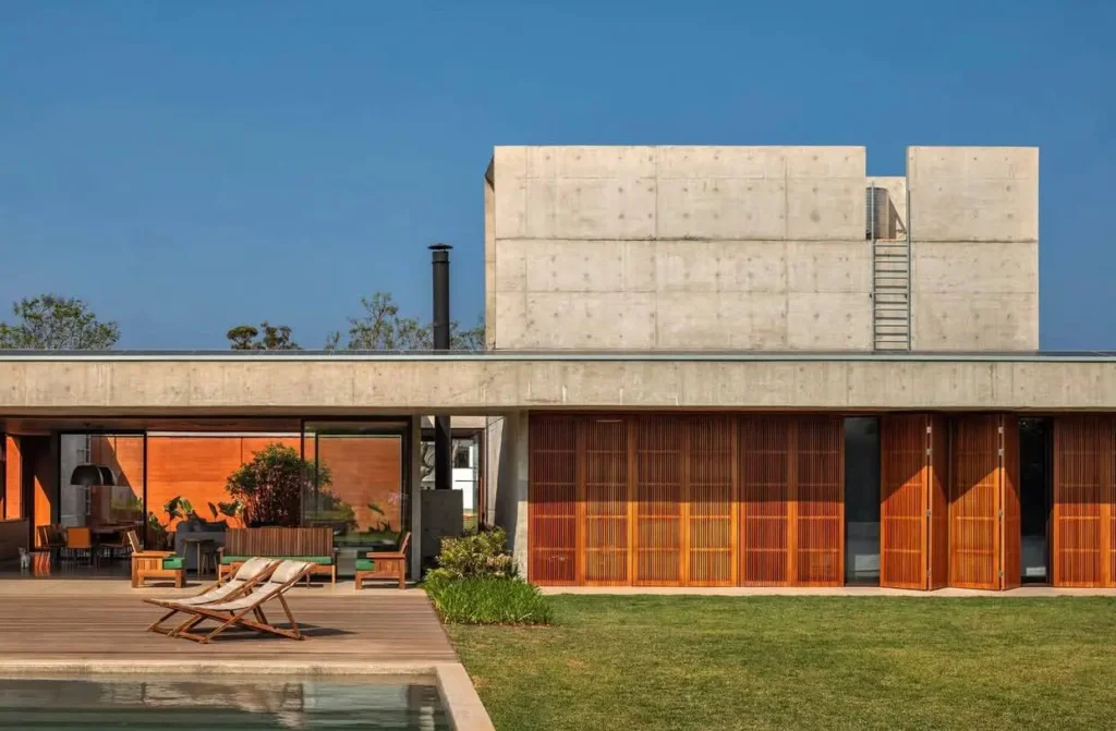 A modern concrete home with a poolside deck and large folding wooden doors that open to the lawn.