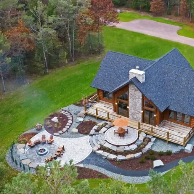 Embracing Grandeur: 25 Inspiring Ideas for Large Log Cabin Homes 18 An aerial view of a modern log cabin with an intricate, multi-level geometric stone patio and fire pit area.
