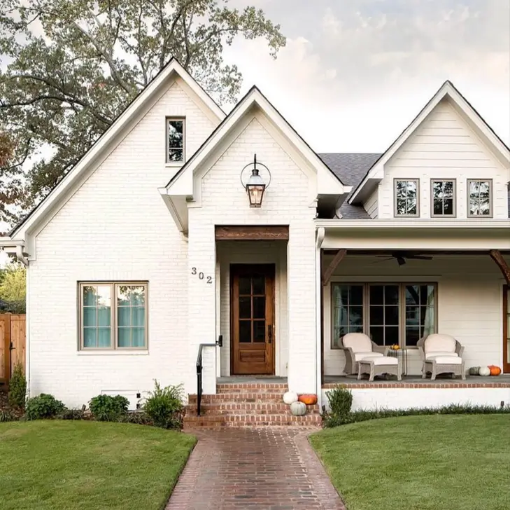 A modern farmhouse with an off-white painted brick exterior, a cozy porch, and a brick walkway.