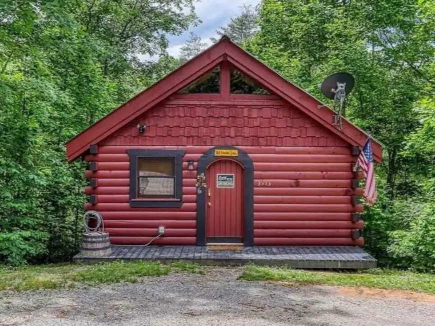Small Log Cabins: 36 Ideas for Cozy Living & Enduring Charm 18 A small red log cabin with black trim nestled amongst dense green trees.