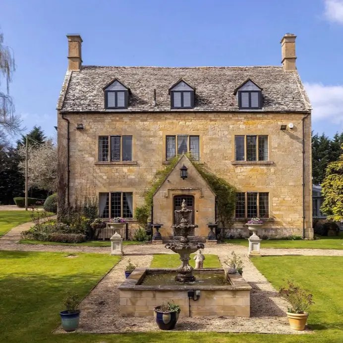 A symmetrical stone country house design with a formal garden and a central tiered water fountain.