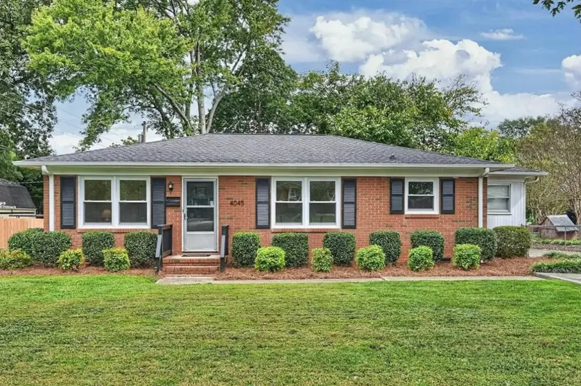 A classic red brick ranch house with black shutters, white trim, and manicured shrubs.