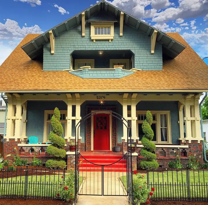 A craftsman house exterior with blue-gray shingles, cream trim, a brick porch, and a vibrant red front door.