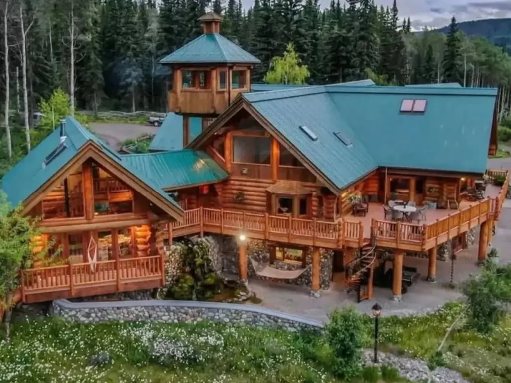 Embracing Grandeur: 25 Inspiring Ideas for Large Log Cabin Homes 19 A large log cabin home with a green metal roof, an observation tower, and an expansive elevated deck with a waterfall below.