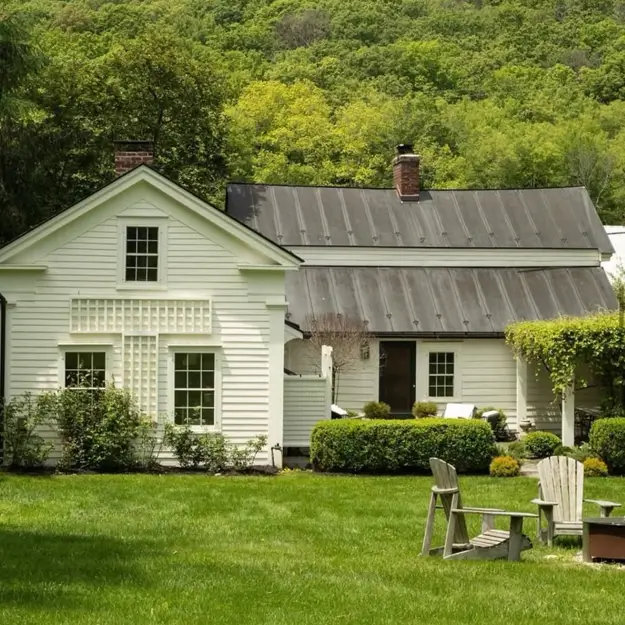 A sophisticated modern country house with white siding, a dark metal roof, and a manicured green lawn.