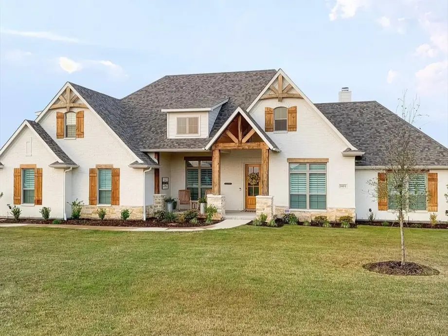 A sprawling off-white brick farmhouse with rustic wood shutters and heavy timber gable accents.