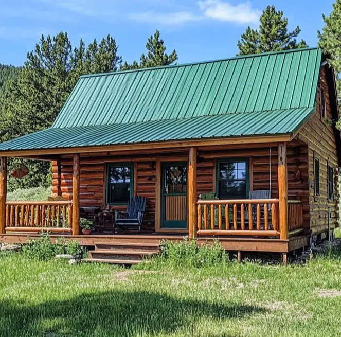 Small Log Cabins: 36 Ideas for Cozy Living & Enduring Charm 19 A small log cabin with a bright green metal roof and a full-length porch in a sunny meadow.