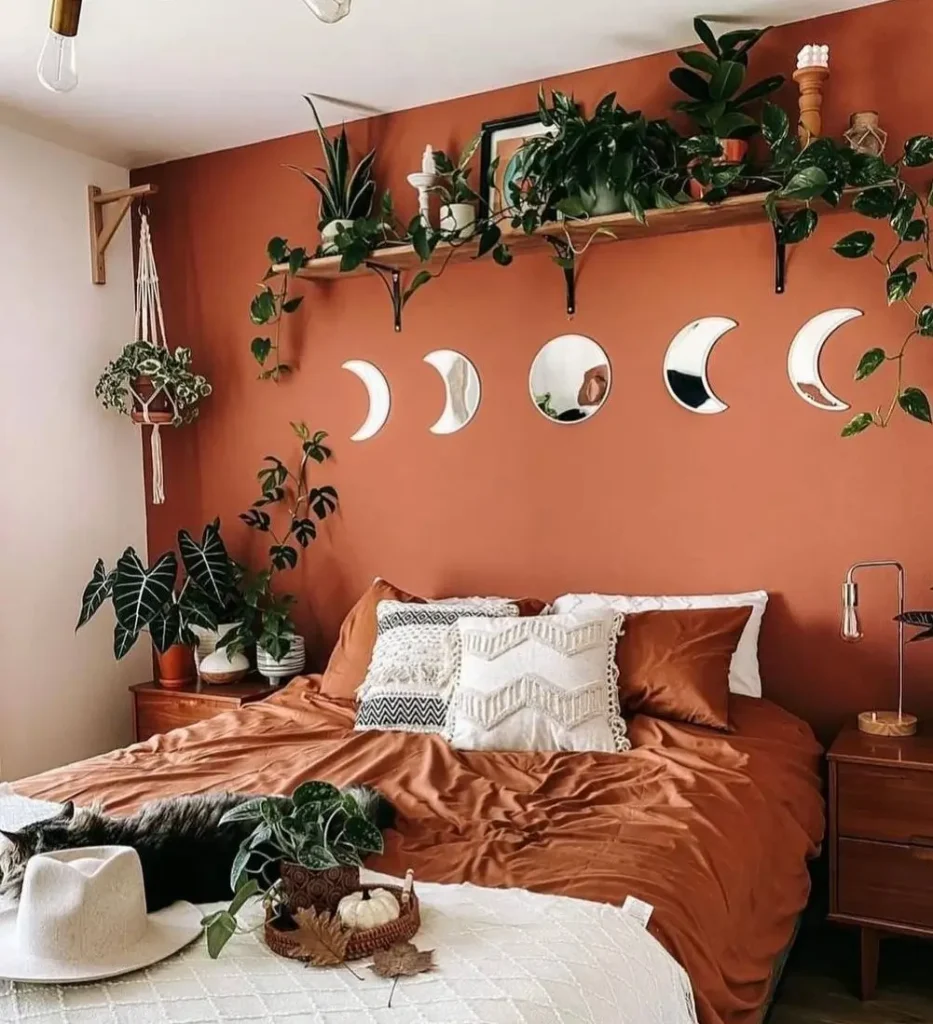 A boho bedroom with a terracotta accent wall featuring a set of mirrored moon phase decals above a bed with matching rust-colored bedding.
