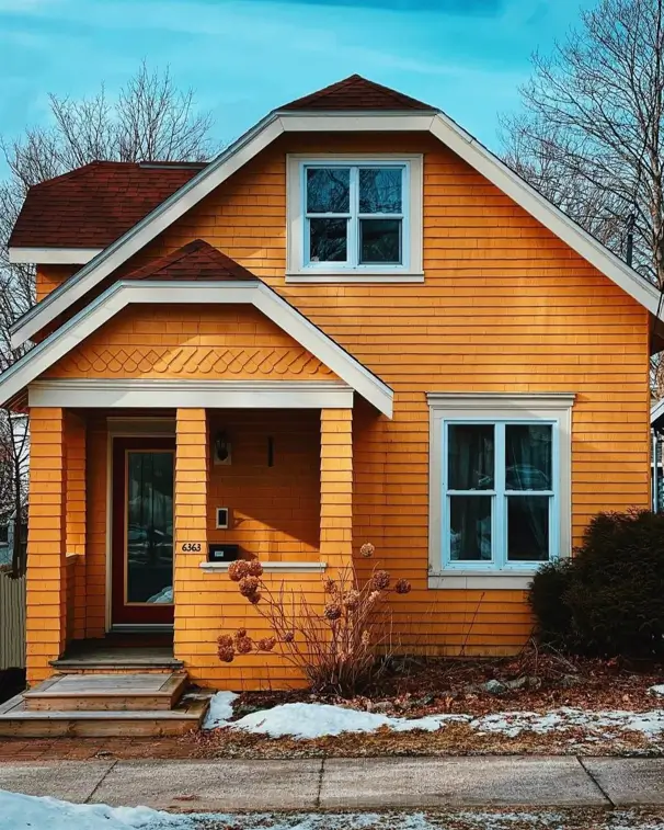 A craftsman-style cottage with bold golden-yellow shingle siding and crisp white trim in a snowy setting.