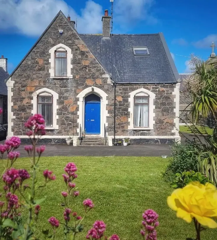 A dark stone cottage with light stone trim around the windows and a bright blue door.