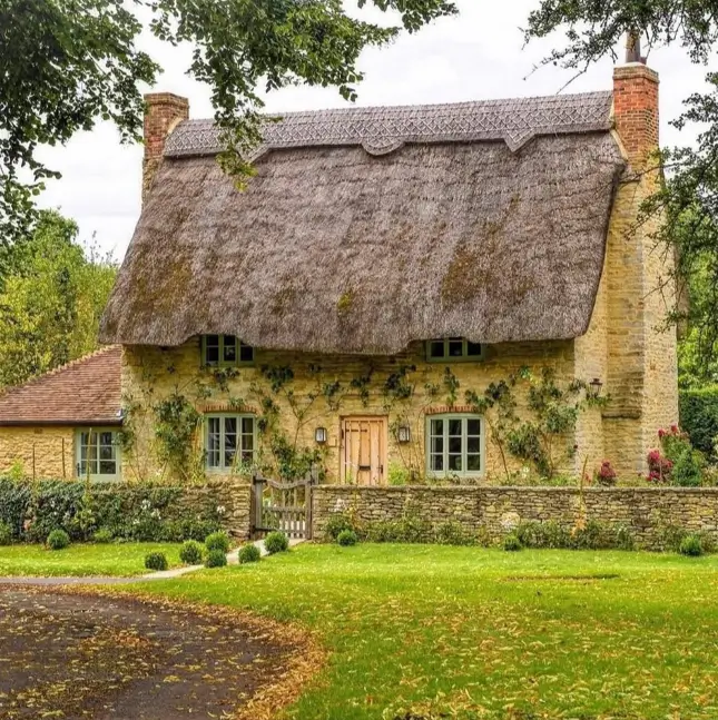 Stone English country home with a traditional thatched roof and a low stone wall.