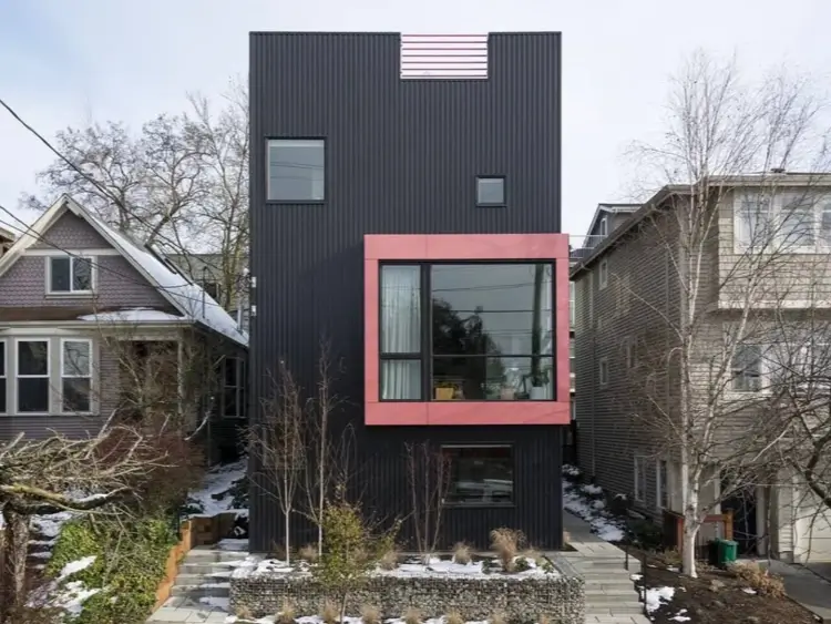 A unique modern black house with corrugated siding and a colorful projecting window frame as an artistic focal point.