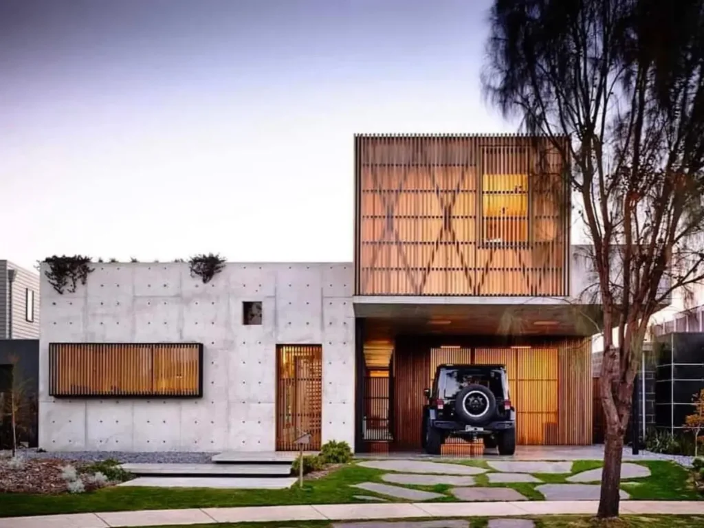 A modern concrete house featuring a board-formed facade and a decorative wooden screen on the second story.