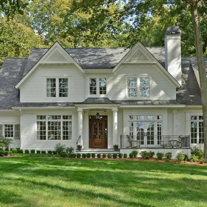 A large, modern country house with an elegant symmetrical design, off-white siding, and a prominent wood front door.