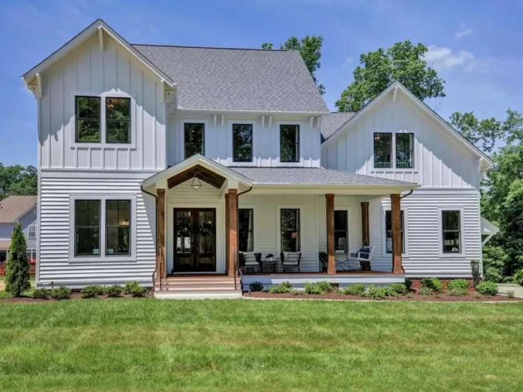 A large off-white modern farmhouse with mixed vertical and horizontal siding and a porch with dark wood posts.
