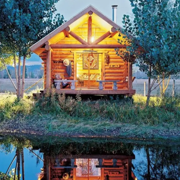 60 Charming Small Log Cabin Ideas to Inspire Your Rustic Retreat 19 A warmly lit small log cabin home at dusk, reflecting perfectly in the calm water in front of it.