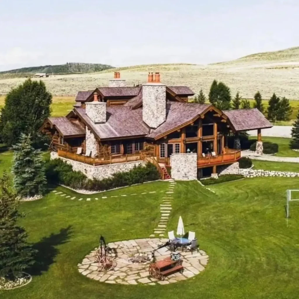 Embracing Grandeur: 25 Inspiring Ideas for Large Log Cabin Homes 21 A sprawling big log cabin home with large stone chimneys and a vast lawn in a wide-open, hilly landscape.