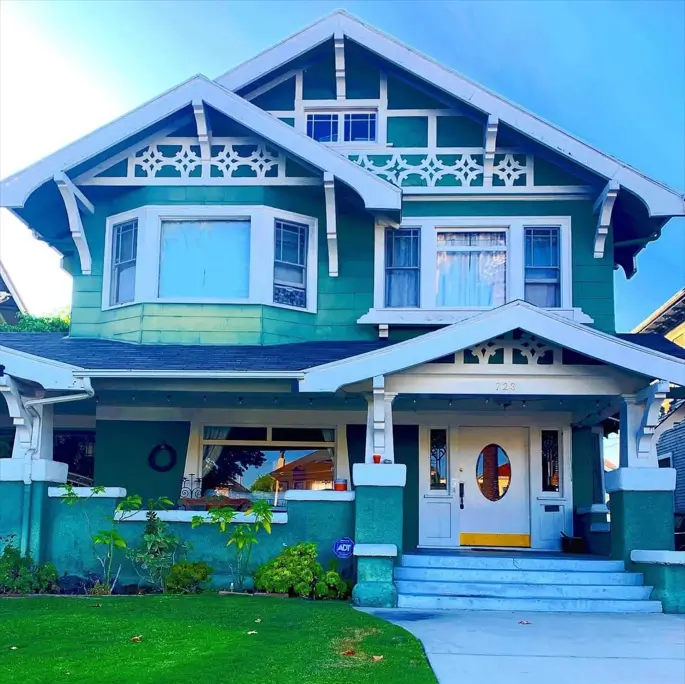 A vibrant green craftsman house exterior with intricate white decorative trim in the gables and a wide front porch.