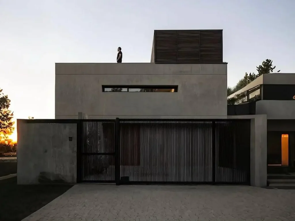 A minimalist modern concrete home at sunset with a long horizontal window and a black slatted gate.